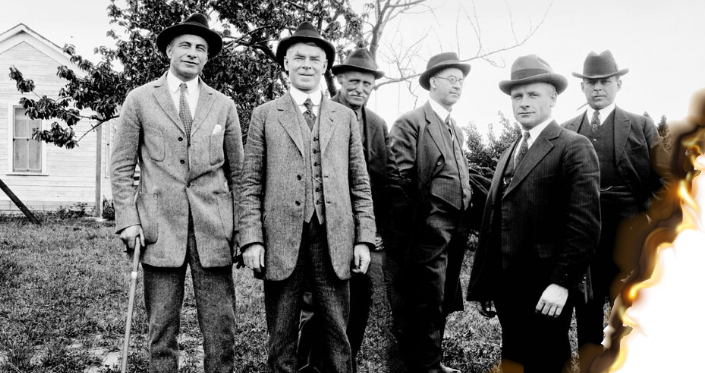 A group of upper-class men in the dress of the early 1920s pose for a photograph; the edges of the photo are on fire.